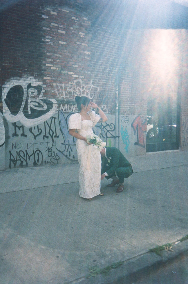 Wedding Photography in NYC, groom kneeling down to help bride with her dress